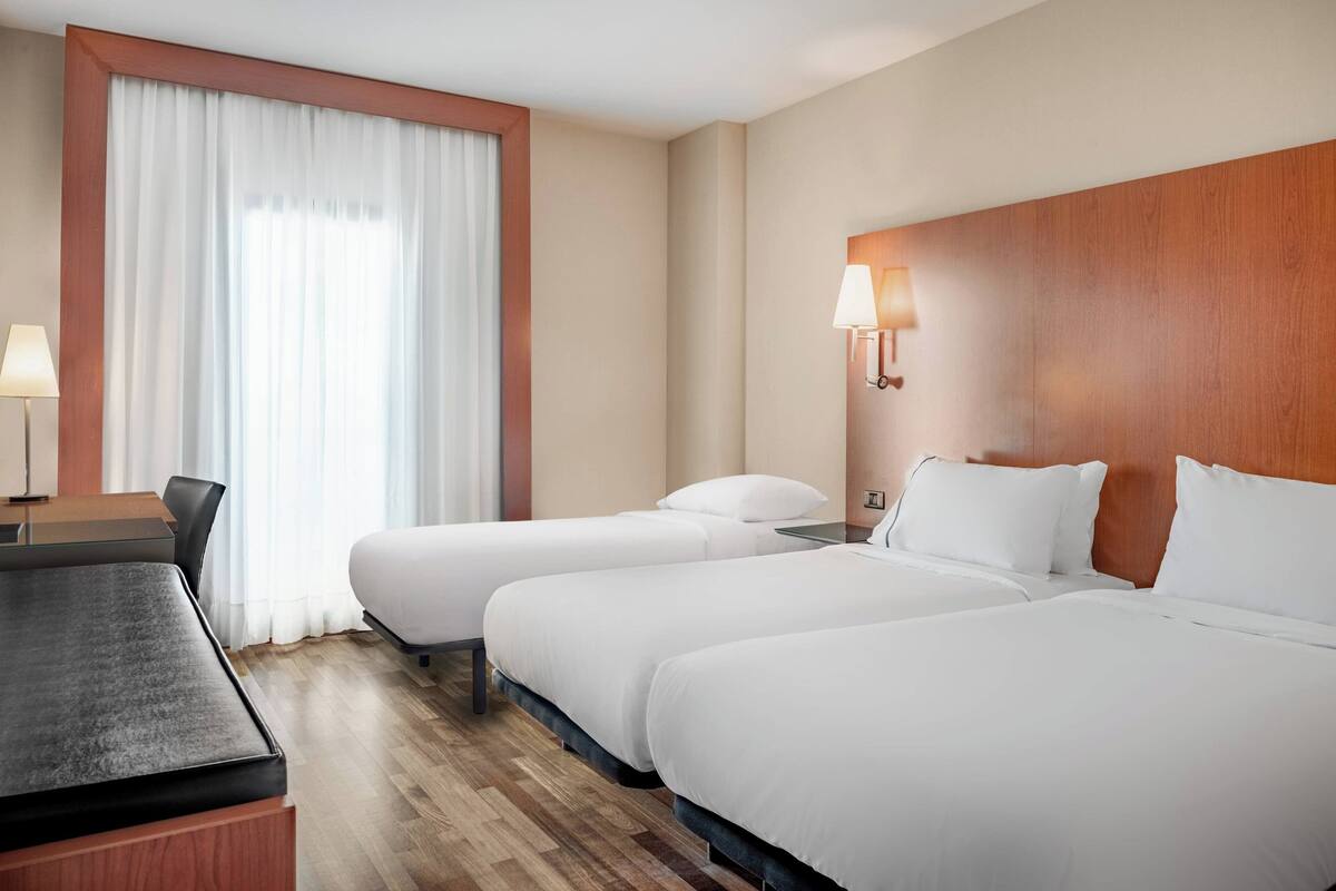 A hotel room with two single beds, a desk, and a chair.