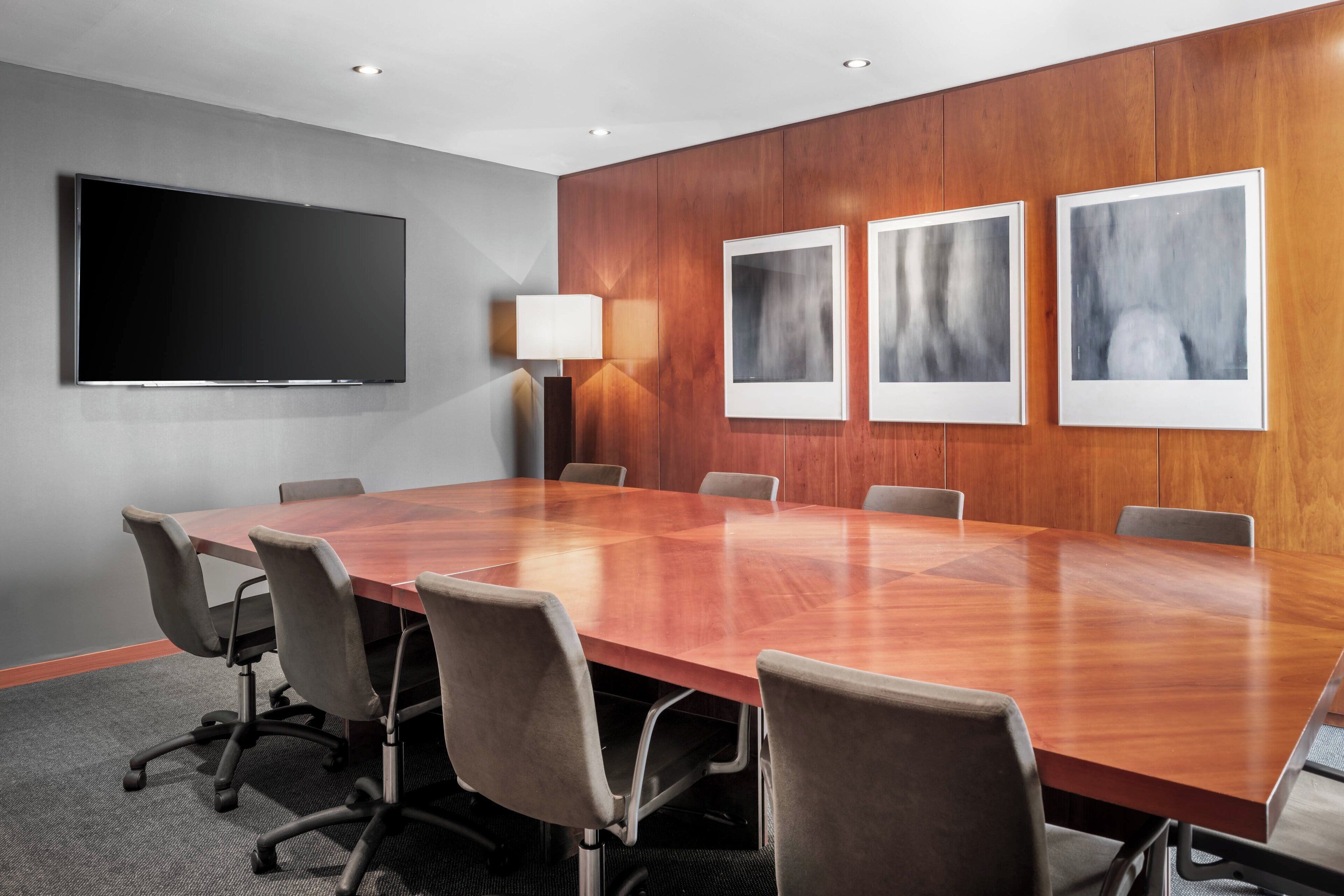 A conference room with a large wooden table, six chairs, a flat-screen TV, and three framed pictures on the wall.