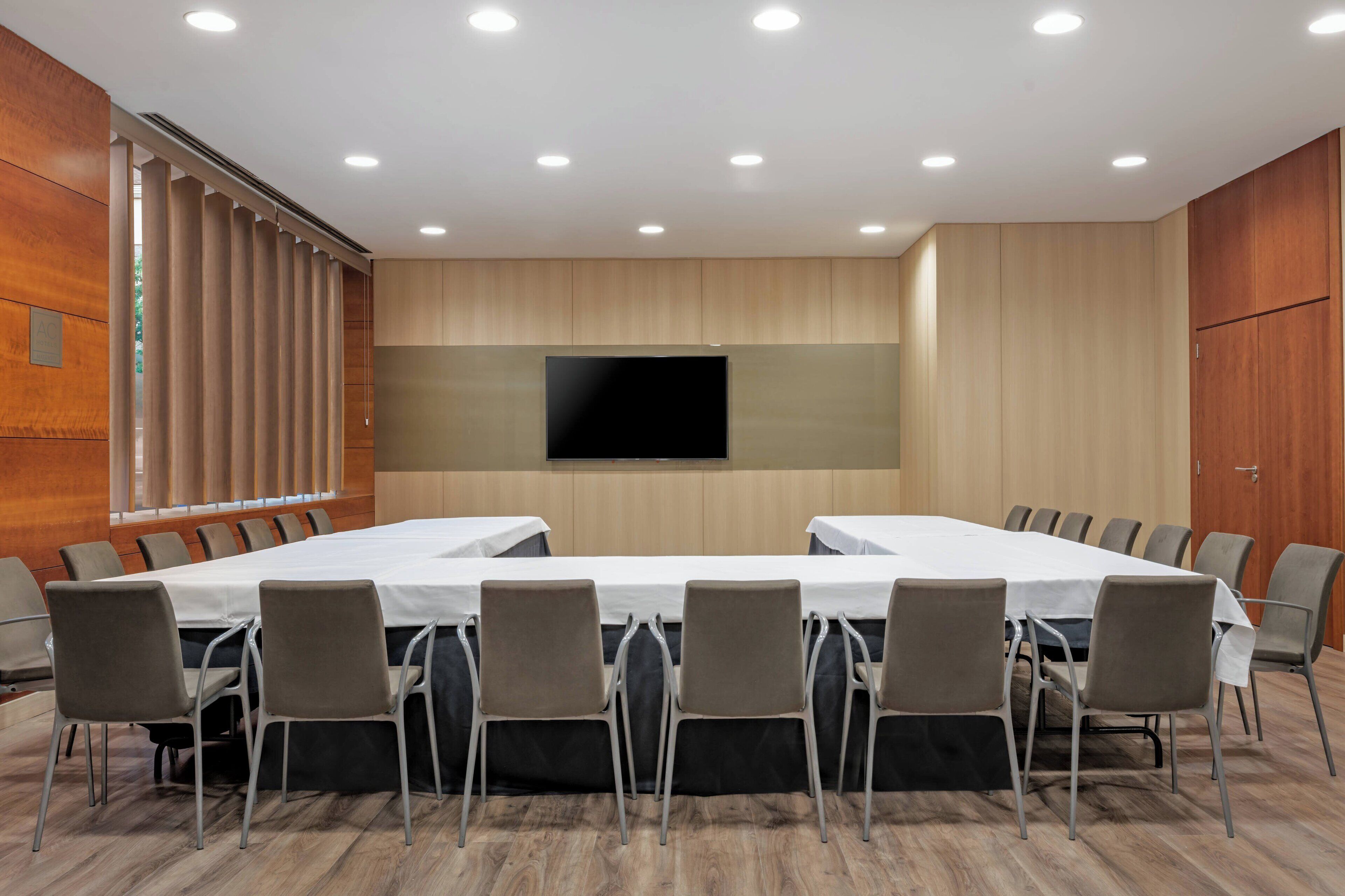 A conference room with a long table, multiple chairs, a flat-screen TV, and wooden paneling.