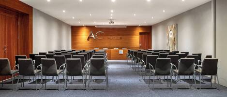 Un salón de conferencias con filas de sillas, un atril y una pared de madera con el logotipo "AC HOTELS".