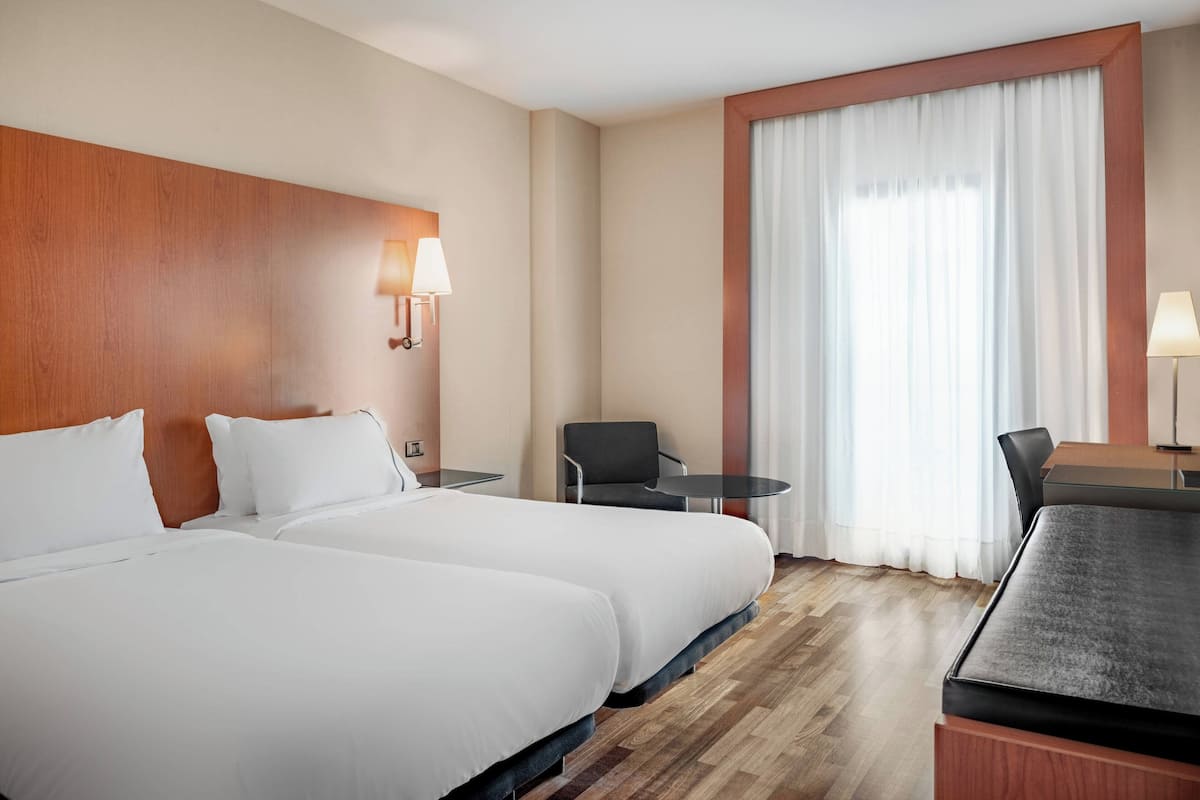 A hotel room with two beds, a small table, a chair, and a desk.