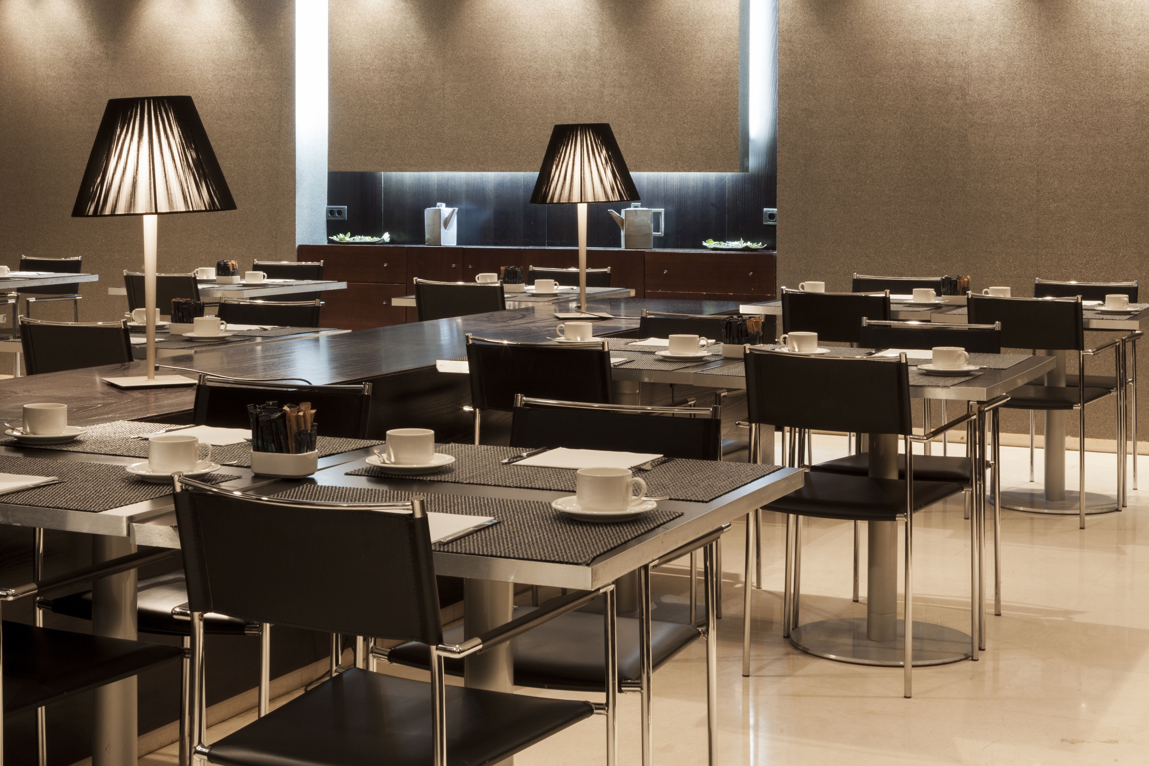 Un comedor de hotel moderno con varias mesas y sillas, equipado con lámparas y montajes de mesa.