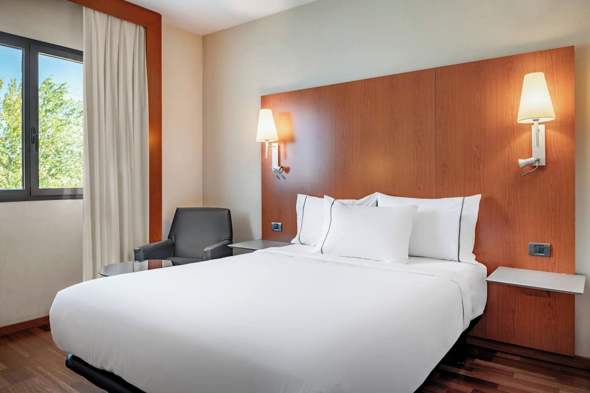 A hotel room with a large bed, two bedside lamps, a chair, and a window with curtains.