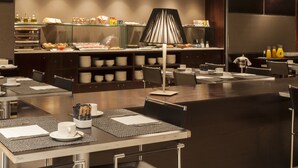 A modern hotel dining area with buffet-style breakfast options, neatly arranged tables, and a central lamp. - AC Hotel Badajoz by Marriott (Badajoz)