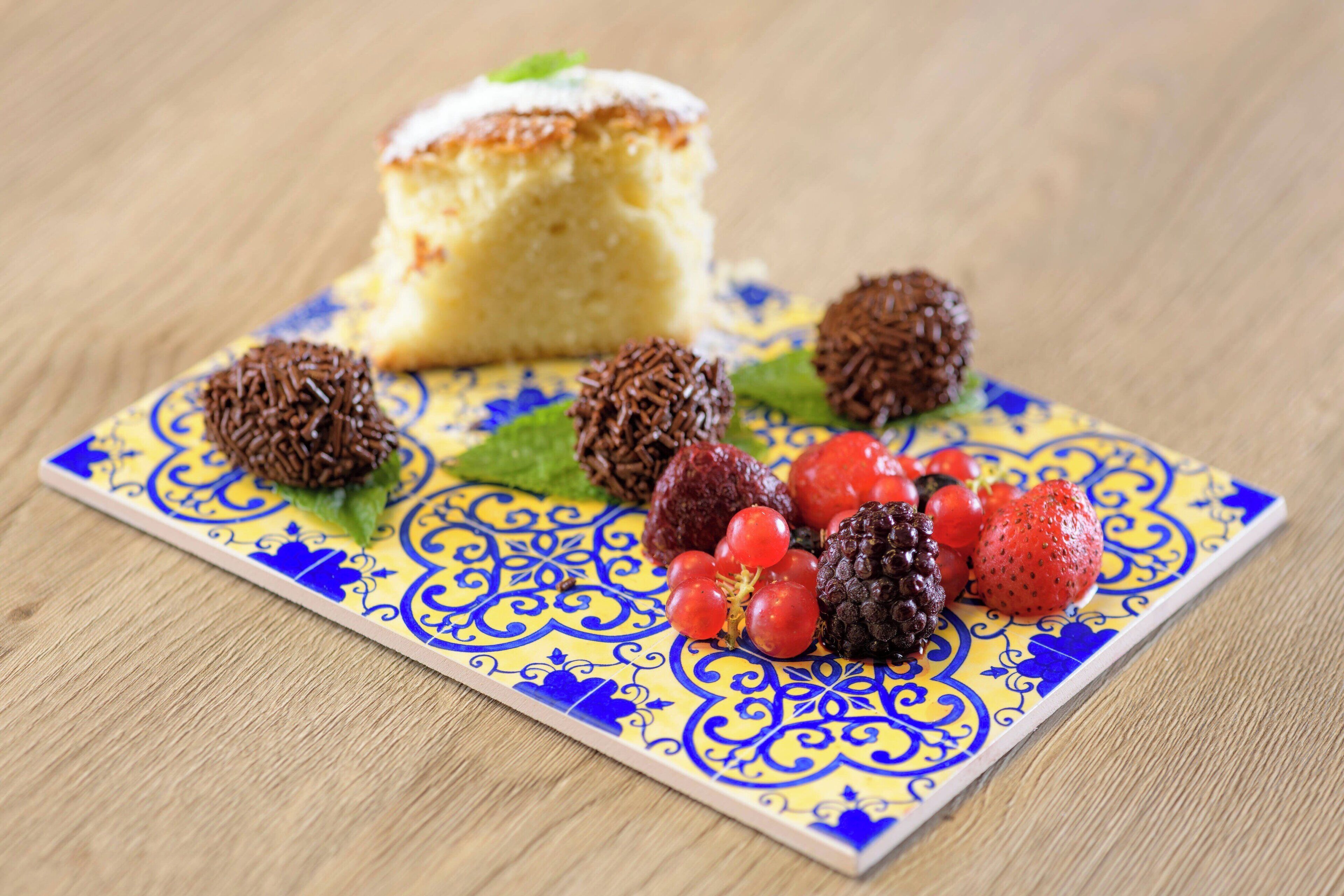 Un plato de postre con una rebanada de pastel, trufas de chocolate y frutos rojos sobre baldosas estampadas.