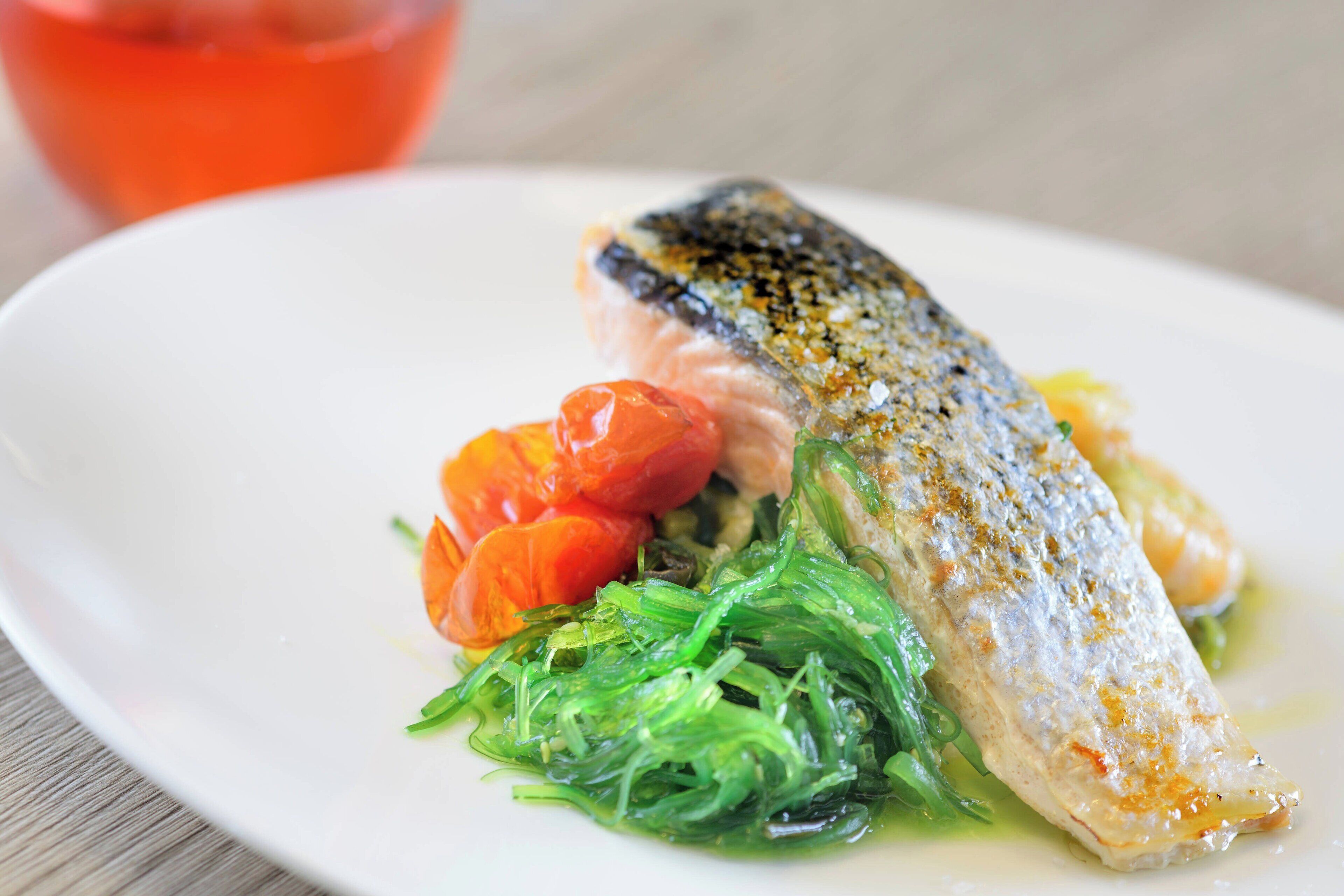 Une assiette blanche avec un poisson, des tomates cerises et des légumes verts.