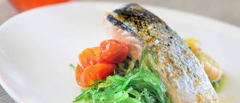 Une assiette blanche avec un poisson, des tomates cerises et des légumes verts.