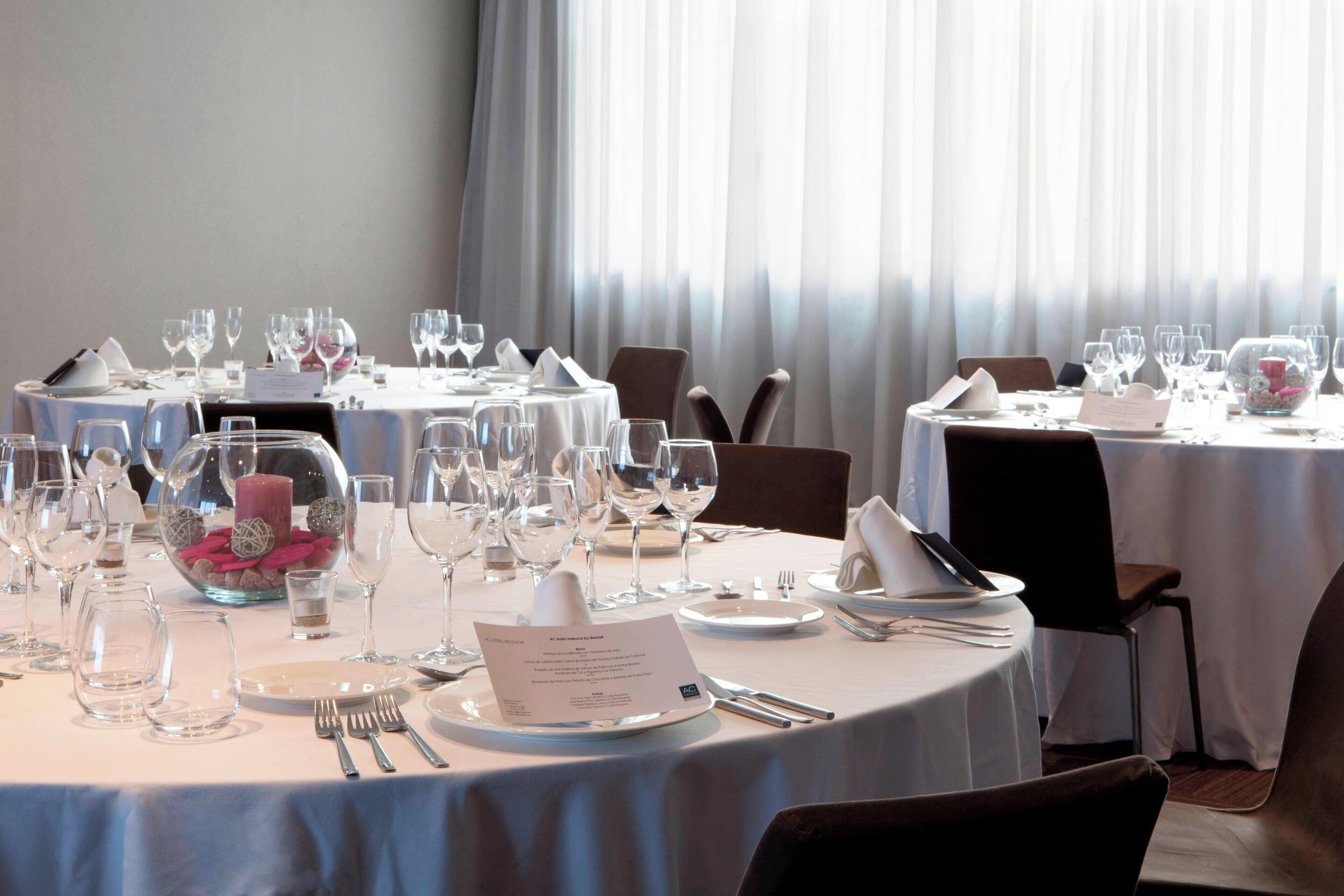 A dining area with round tables set for a meal, each with plates, cutlery, and glasses.