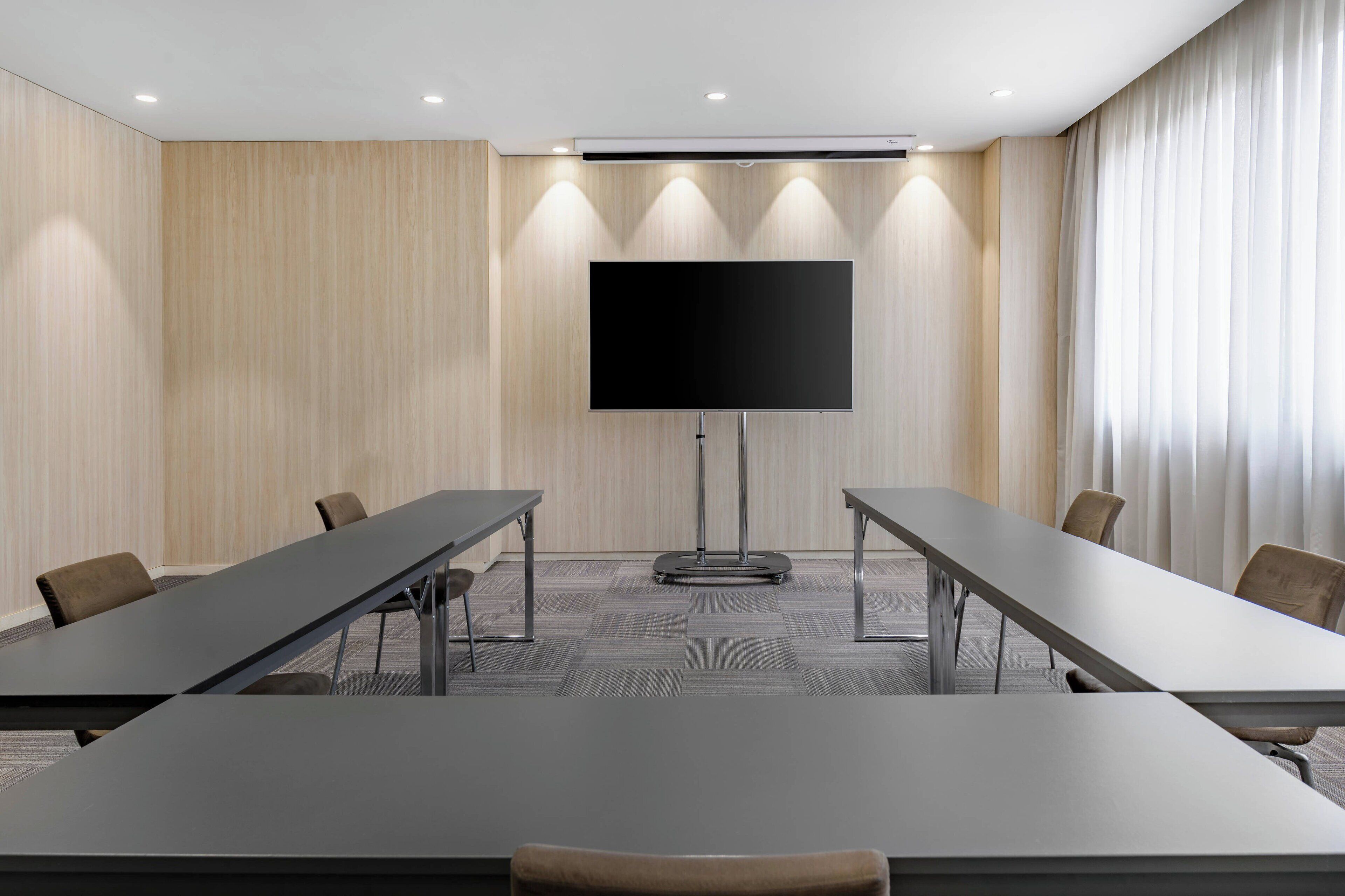 A conference room with a large flat-screen TV, long tables, and chairs.