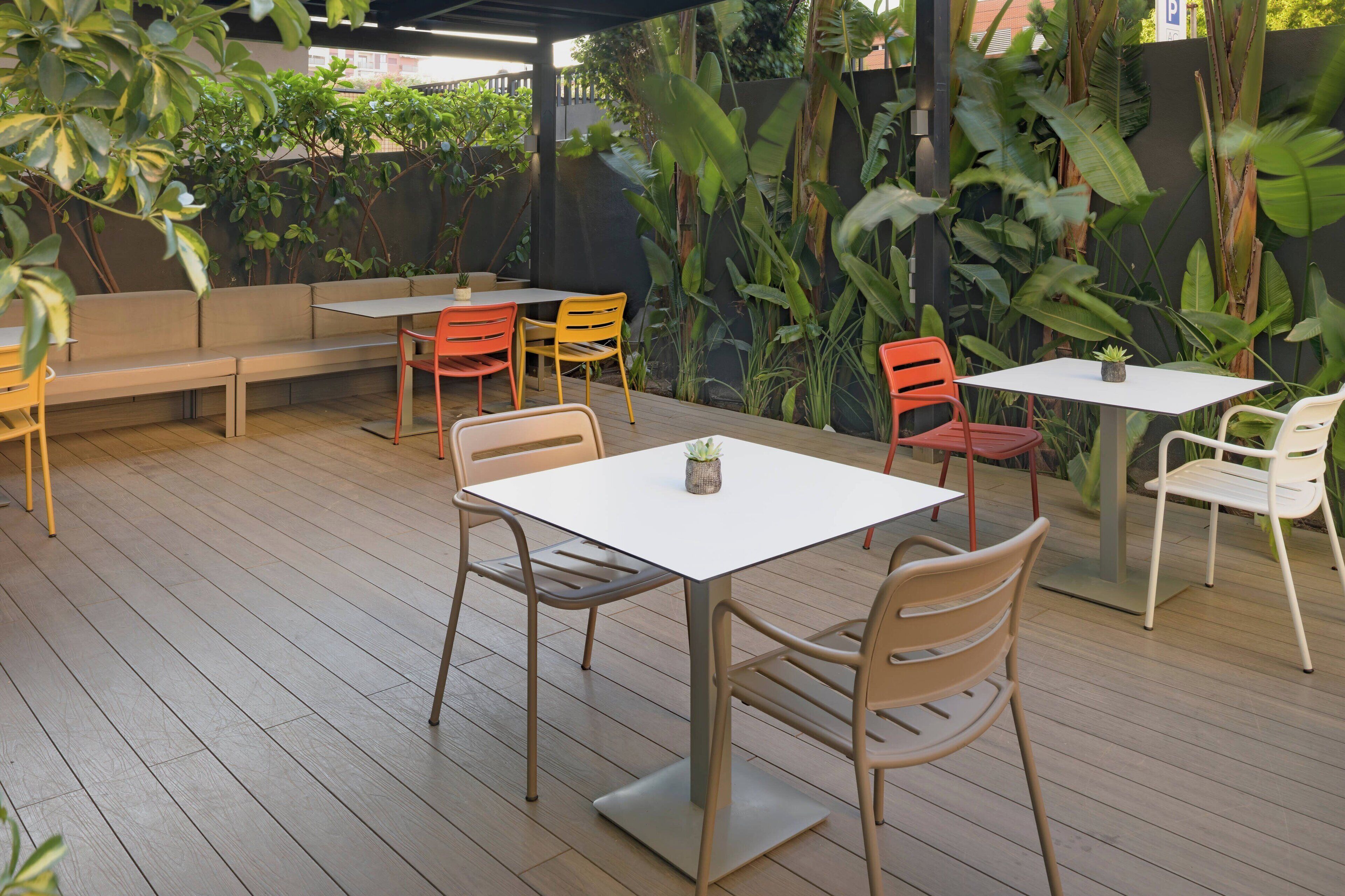 Une terrasse extérieure dotée d’un plancher en bois, d’un aménagement comprenant un banc et des tables, ainsi que de différents types de chaises.