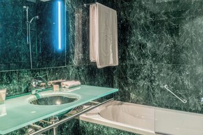 Un baño moderno con un lavabo de cristal, una bañera y una pared de mármol.
