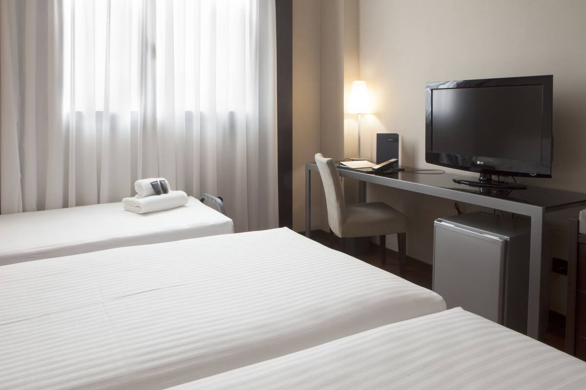 A hotel room with two beds, a desk with a computer and lamp, and a TV.