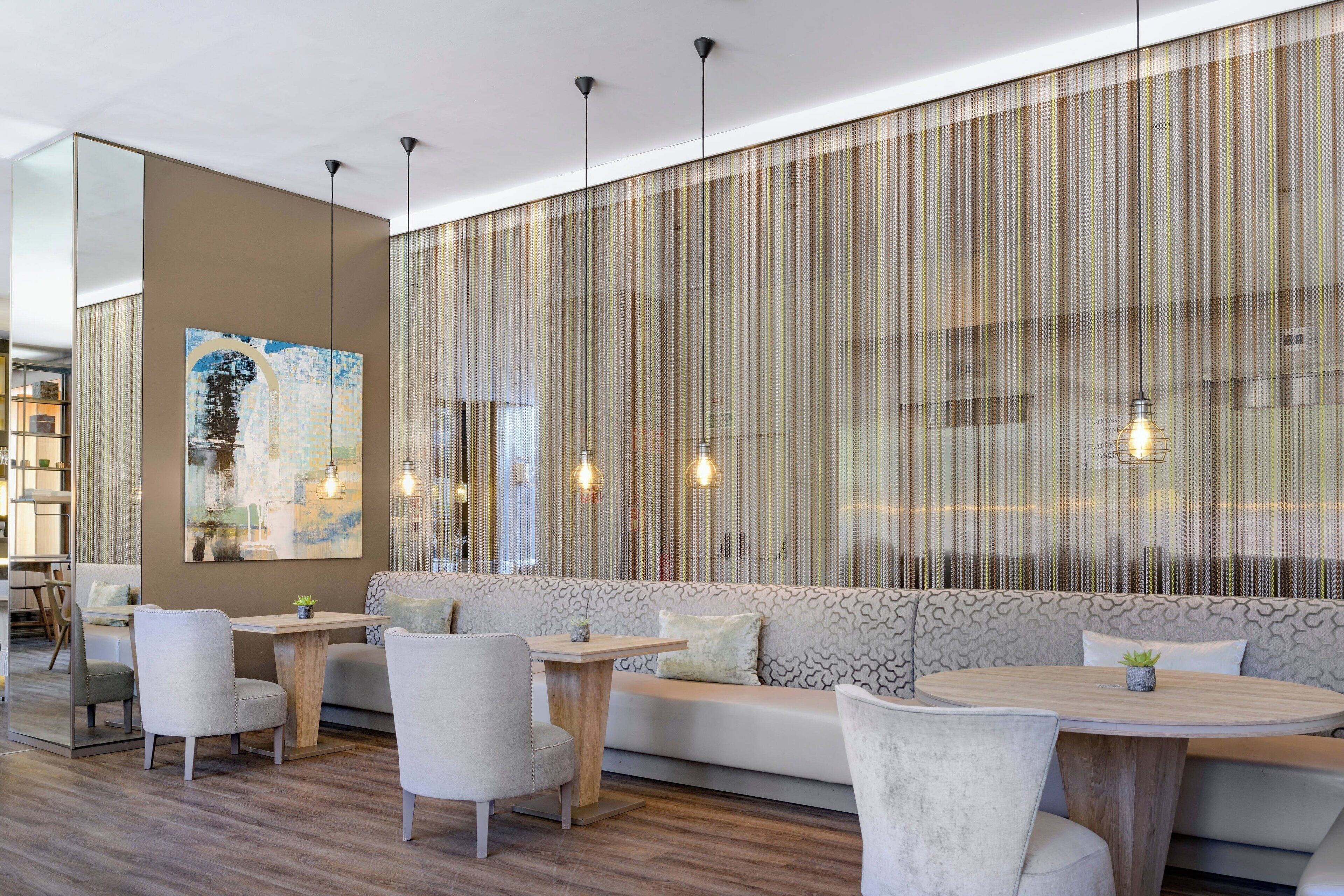 Un interior moderno con una zona de estar, mesas de madera e iluminación colgante.