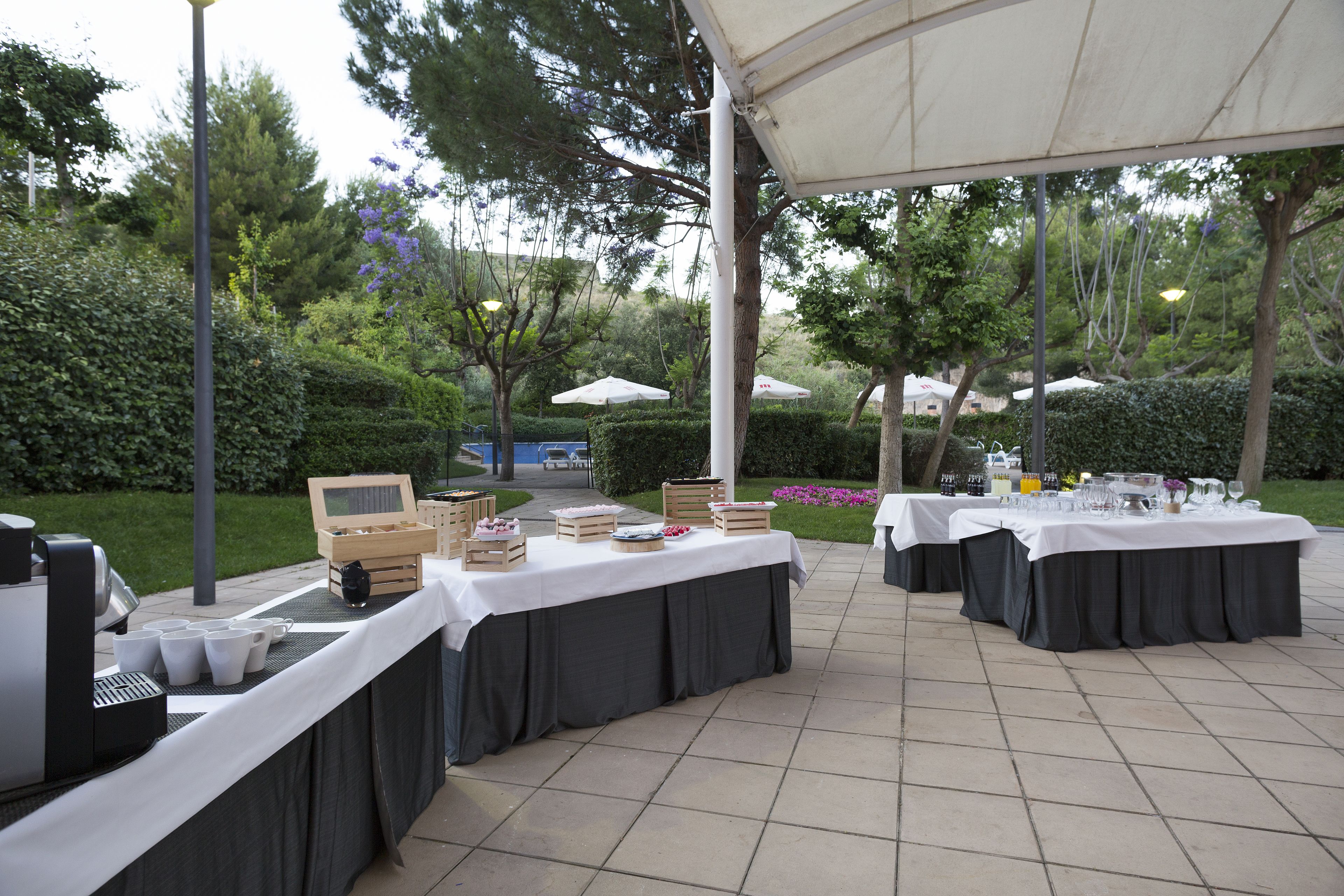 Een open evenementenruimte met tafels klaar voor een diner, omgeven door groen en bomen.