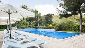 A swimming pool with lounge chairs and umbrellas, surrounded by greenery and a hilly landscape. - Abba Garden (Esplugues de Llobregat)