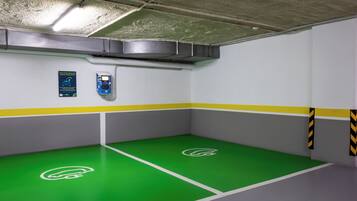 Un estacionamiento con marcas en el suelo de color verde, una estación de carga y un letrero que indica un lugar de estacionamiento reservado para vehículos eléctricos.