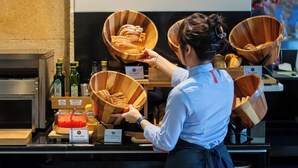 A person arranging bread in wooden bowls on a counter with labels indicating different types of bread and condiments. - Abba Garden (Esplugues de Llobregat)