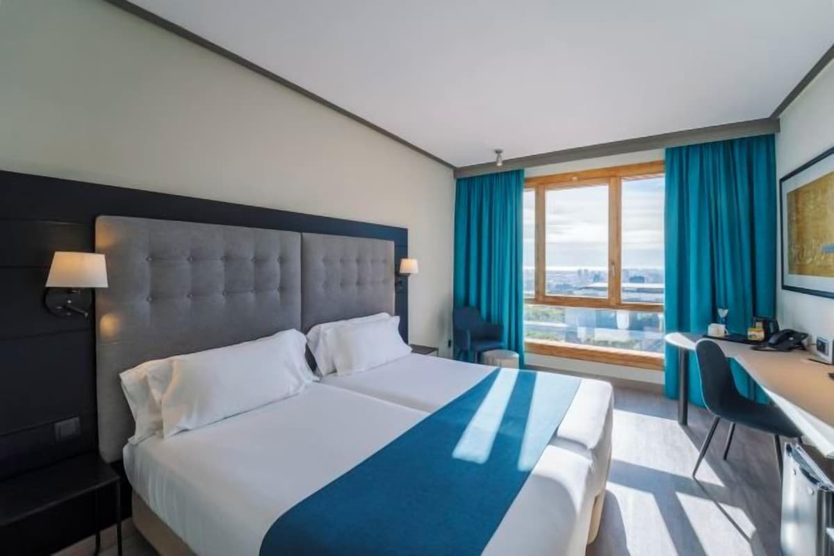 A hotel room with a large bed, a desk, and a view of the city.