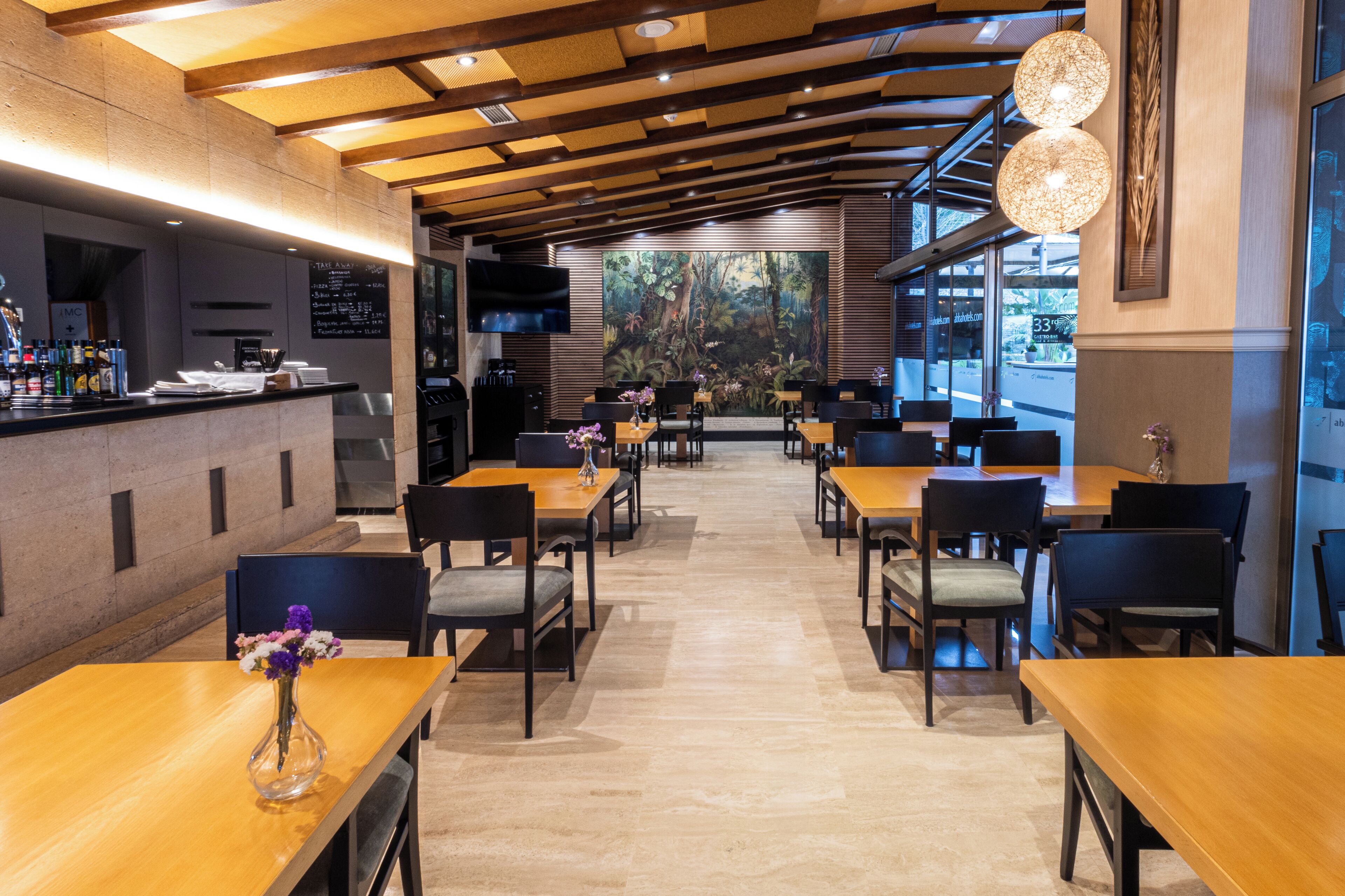 Een modern restaurant met houten tafels en stoelen, een bar en een grote muurschildering van een bos.