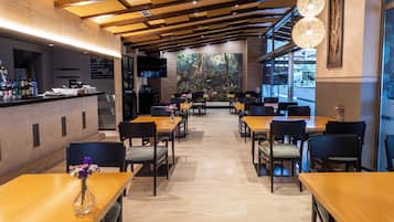 Een modern restaurant met houten tafels en stoelen, een bar en een grote muurschildering van een bos.