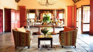 A spacious lobby with a chandelier, two patterned armchairs, a central table with a vase, and a buffet setup in the background. - Pestana Kruger Lodge (Nkomazi)