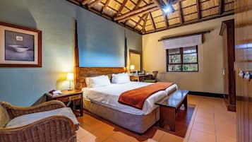 A hotel room with a bed, a bench, wicker furniture, a wooden ceiling, a window, and a framed picture on the wall.