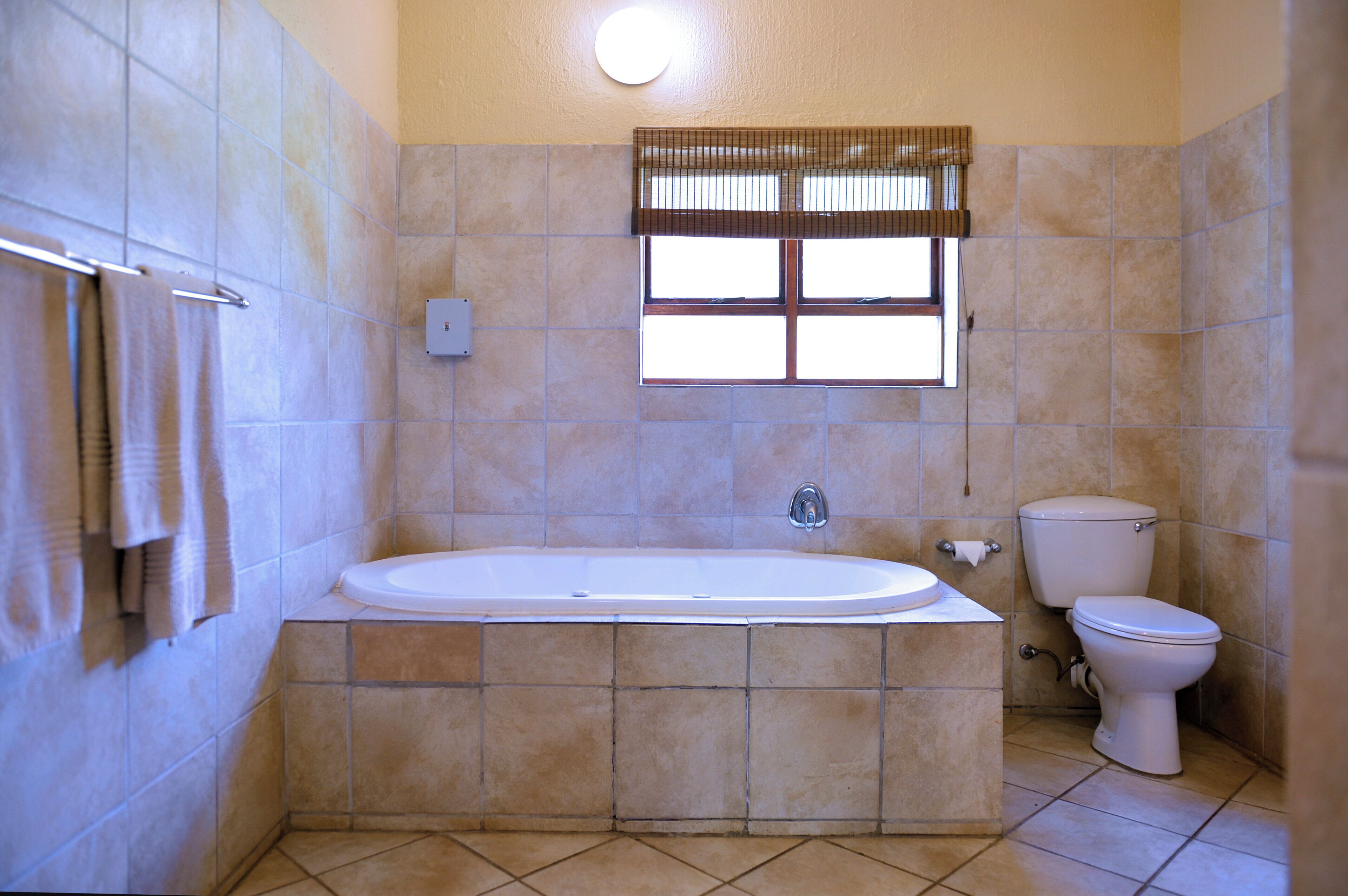 A bathroom with a bathtub, toilet, and a window with blinds.