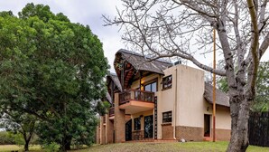 A house with a balcony, a large tree in the yard, and a brick exterior. - Pestana Kruger Lodge (Nkomazi)