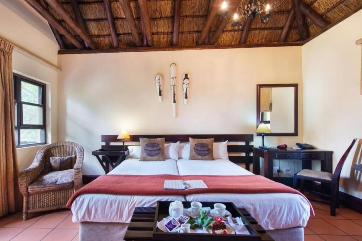 A hotel room with a bed, a chair, a desk, a tray with breakfast, and a chandelier.