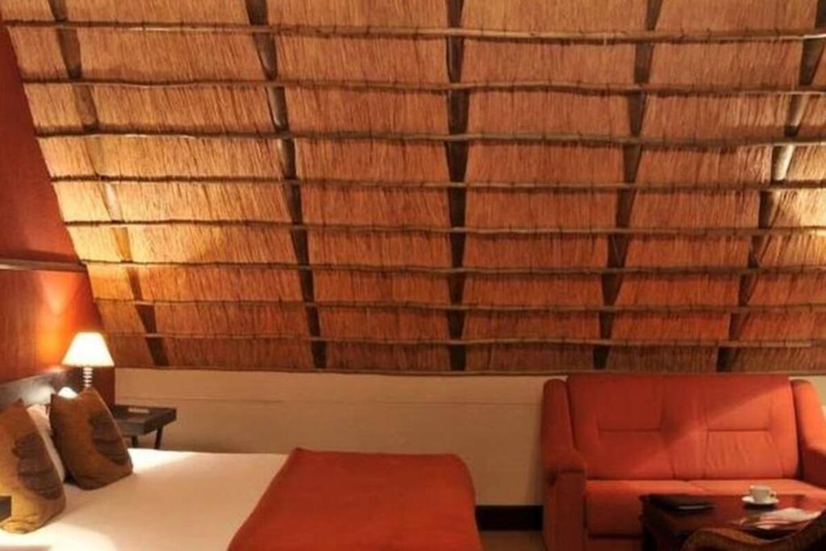 A hotel room with a bed, a sofa, a nightstand with a lamp, and a wall with a woven pattern.