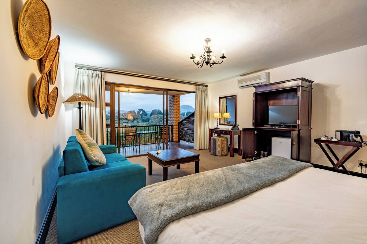 A hotel room with a bed, a sofa, a desk, a TV, and a balcony with a view.