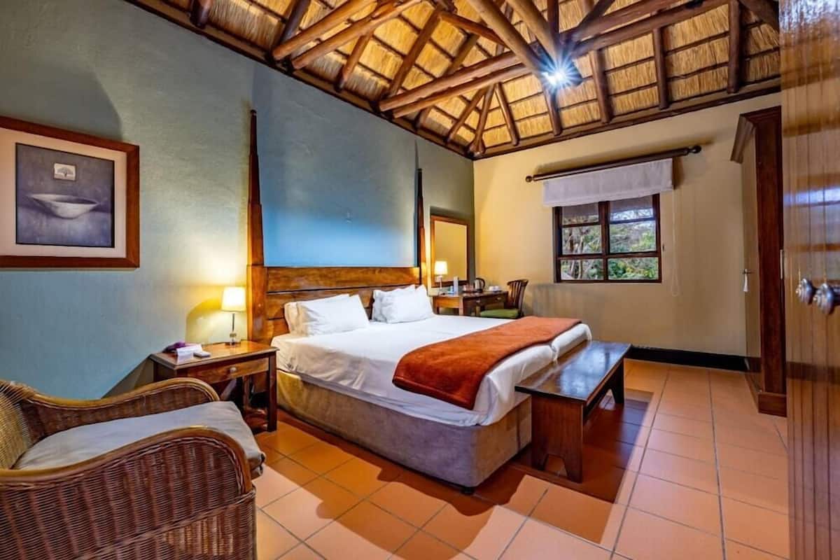 A room with a bed, a wicker chair, a desk, a window, and a wooden ceiling.
