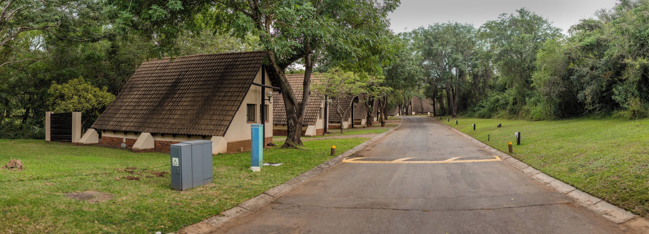 A row of cabins with pitched roofs, a paved road, and surrounding greenery.