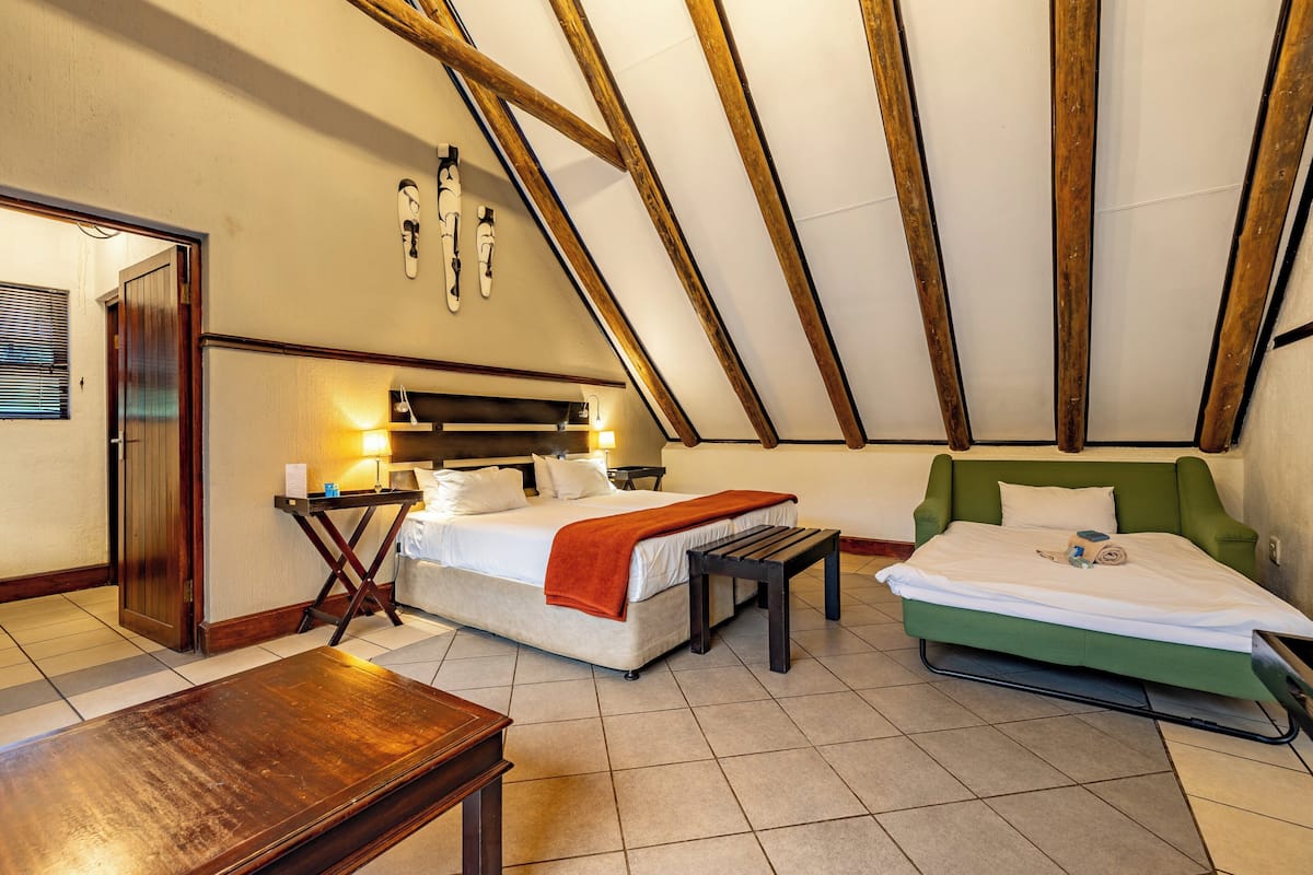 A room with a sloped ceiling, two beds, a wooden table, and a wall-mounted light fixture.