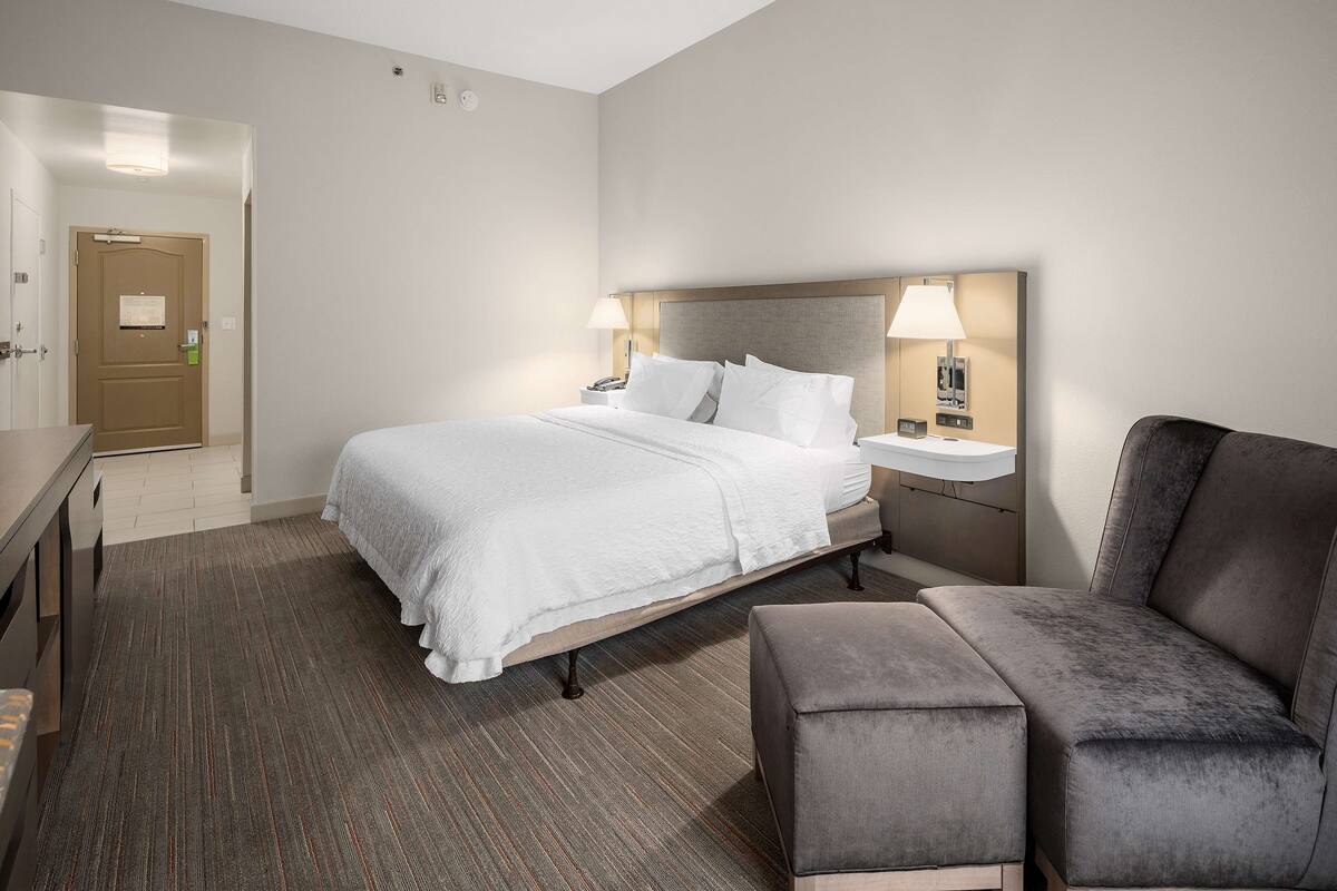 A hotel room with a bed, bedside tables, a chair, and a desk.