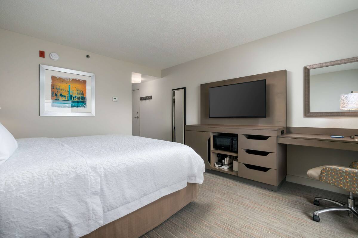 A hotel room with a bed, a TV, a desk, and a chair.