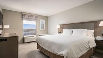 Et hotelværelse med en stor seng, et skrivebord, en lampe, et natbord og et vindue med udsigt.