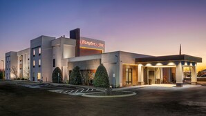 Un moderno hotel Hampton Inn con un letrero llamativo, un acceso cubierto y un estacionamiento.