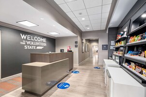 Uma área de recepção moderna com um letreiro 'Welcome to the Volunteer State', um balcão de atendimento e um bar de lanches com diversos alimentos.