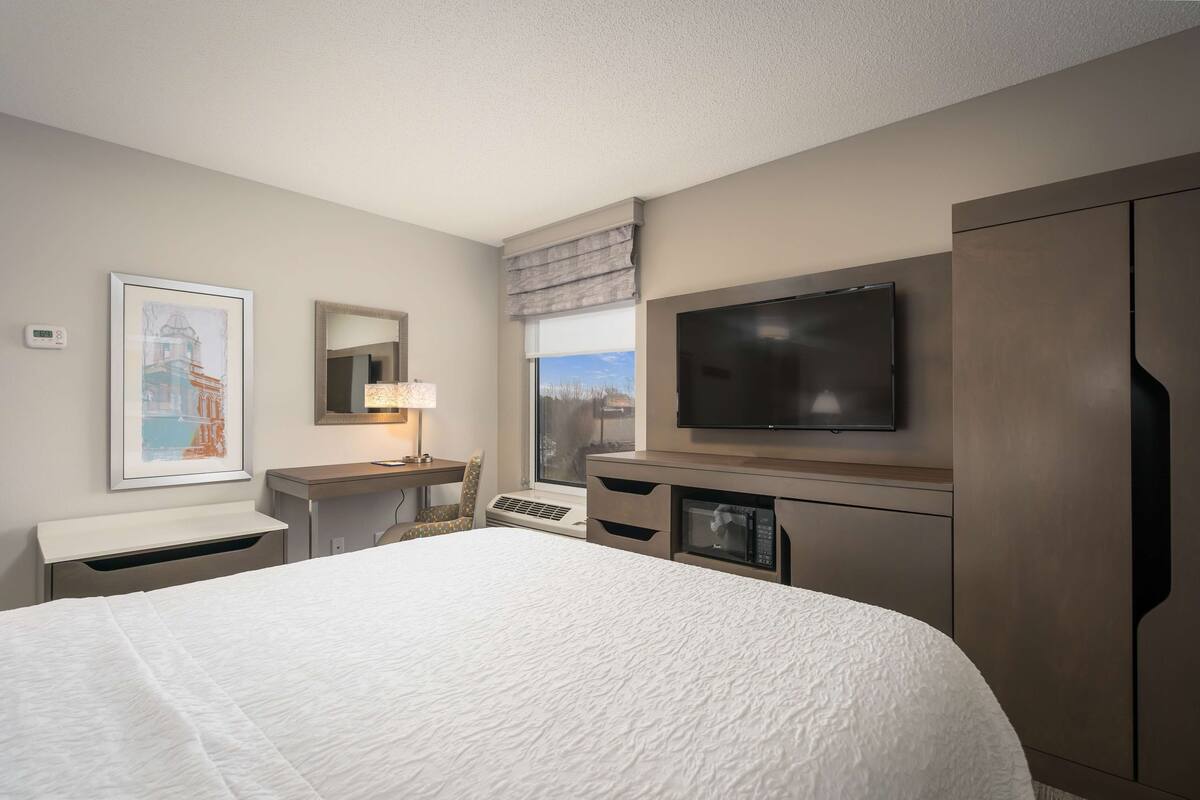 A hotel room with a large bed, a desk with a lamp, a television, and a view of the outdoors.