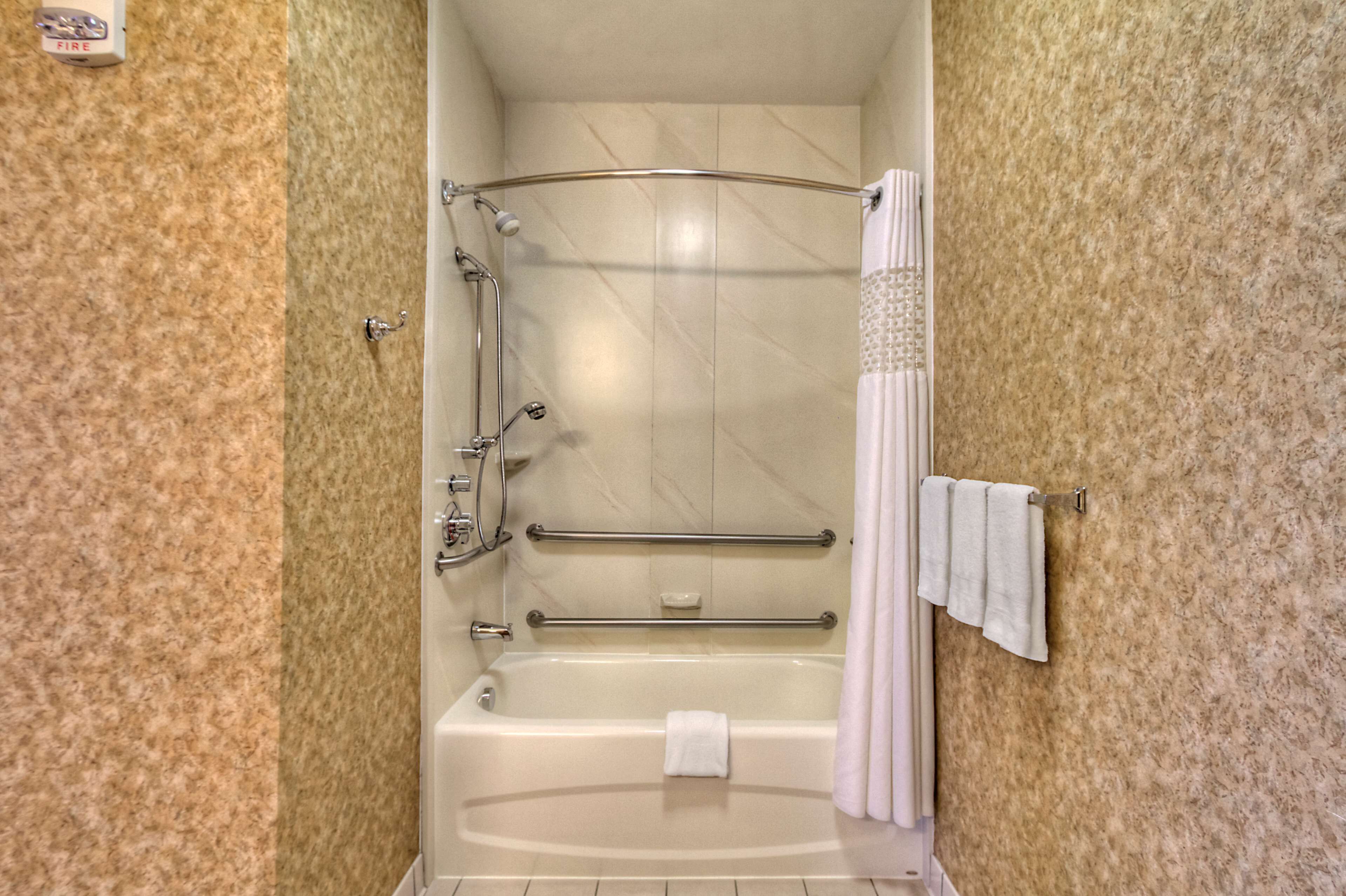 Un baño con bañera, ducha con mampara de vidrio curva y barra de apoyo.