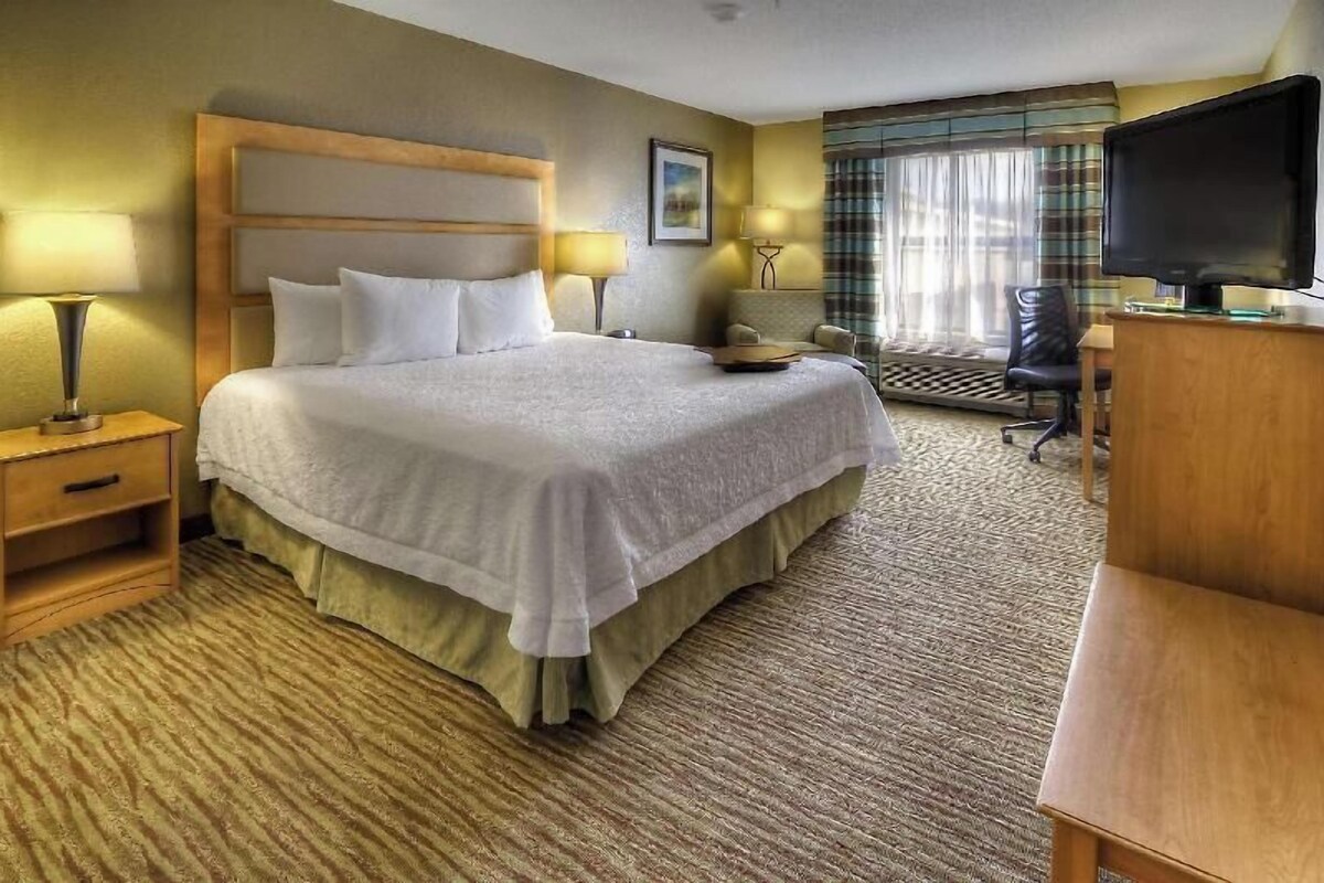 A hotel room with a bed, a desk, a television, and a window with curtains.