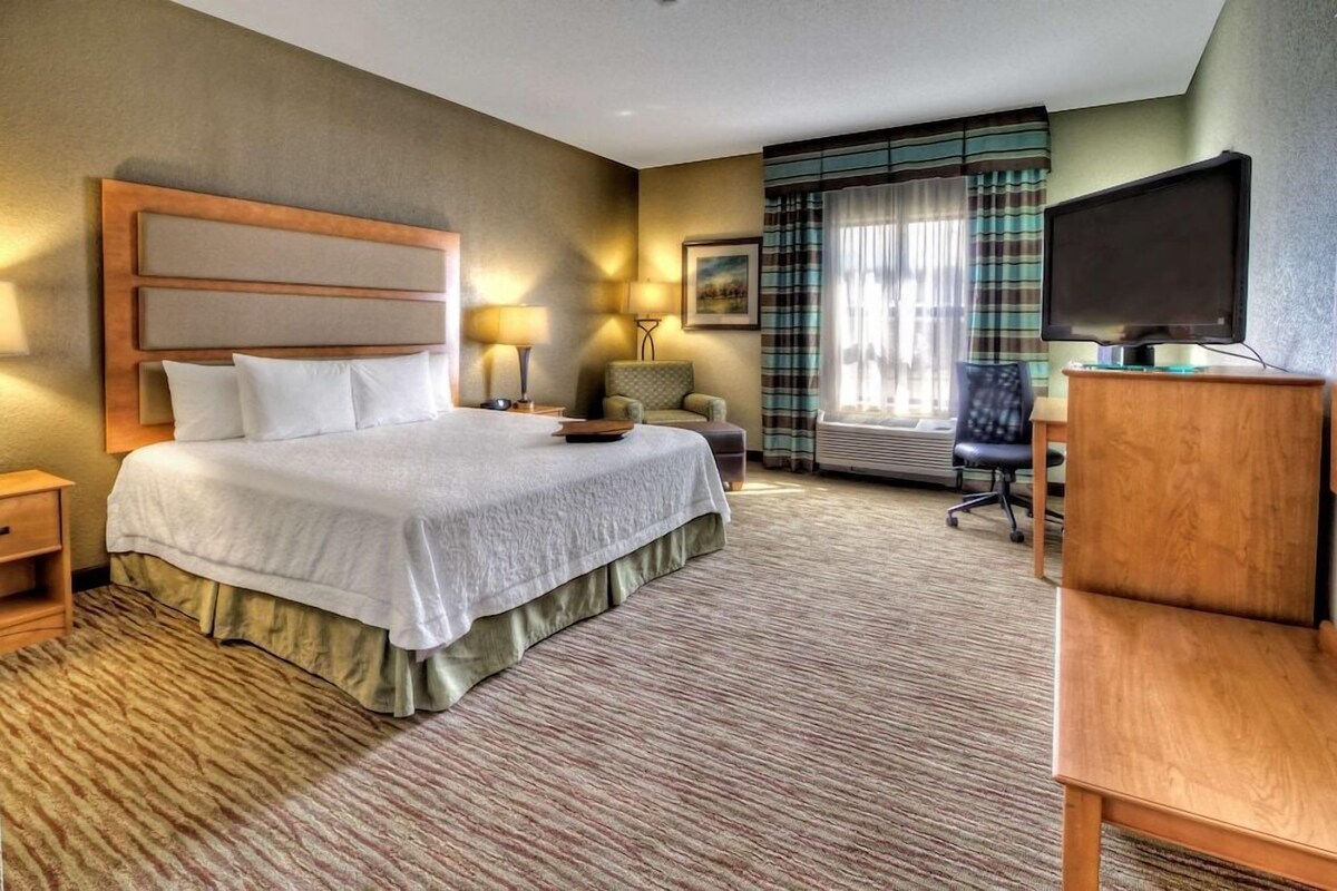 A hotel room with a large bed, a desk, a chair, a television, and a window with curtains.