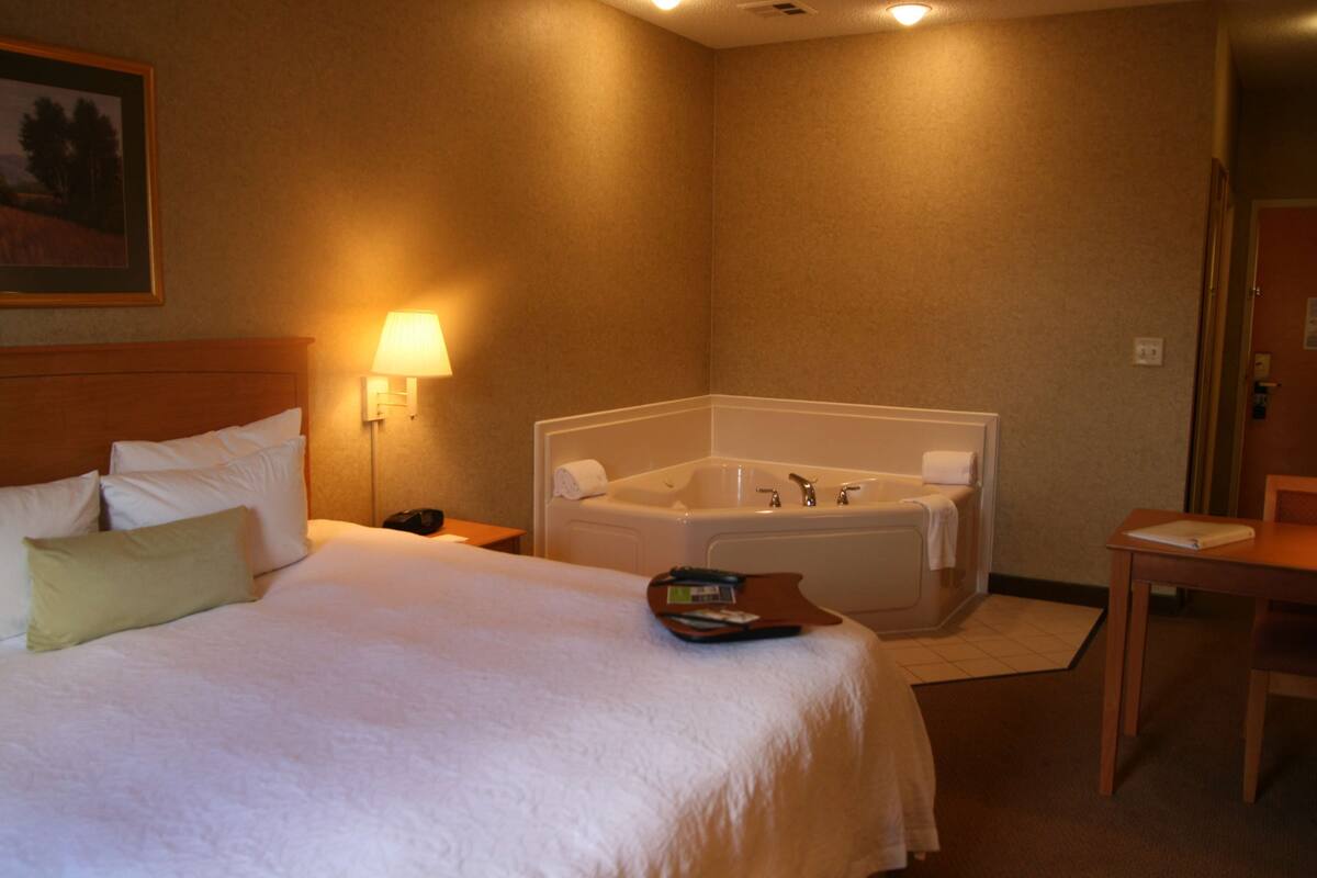 Una habitación de hotel con una cama grande, un rincón de descanso con una mesa y una bañera.