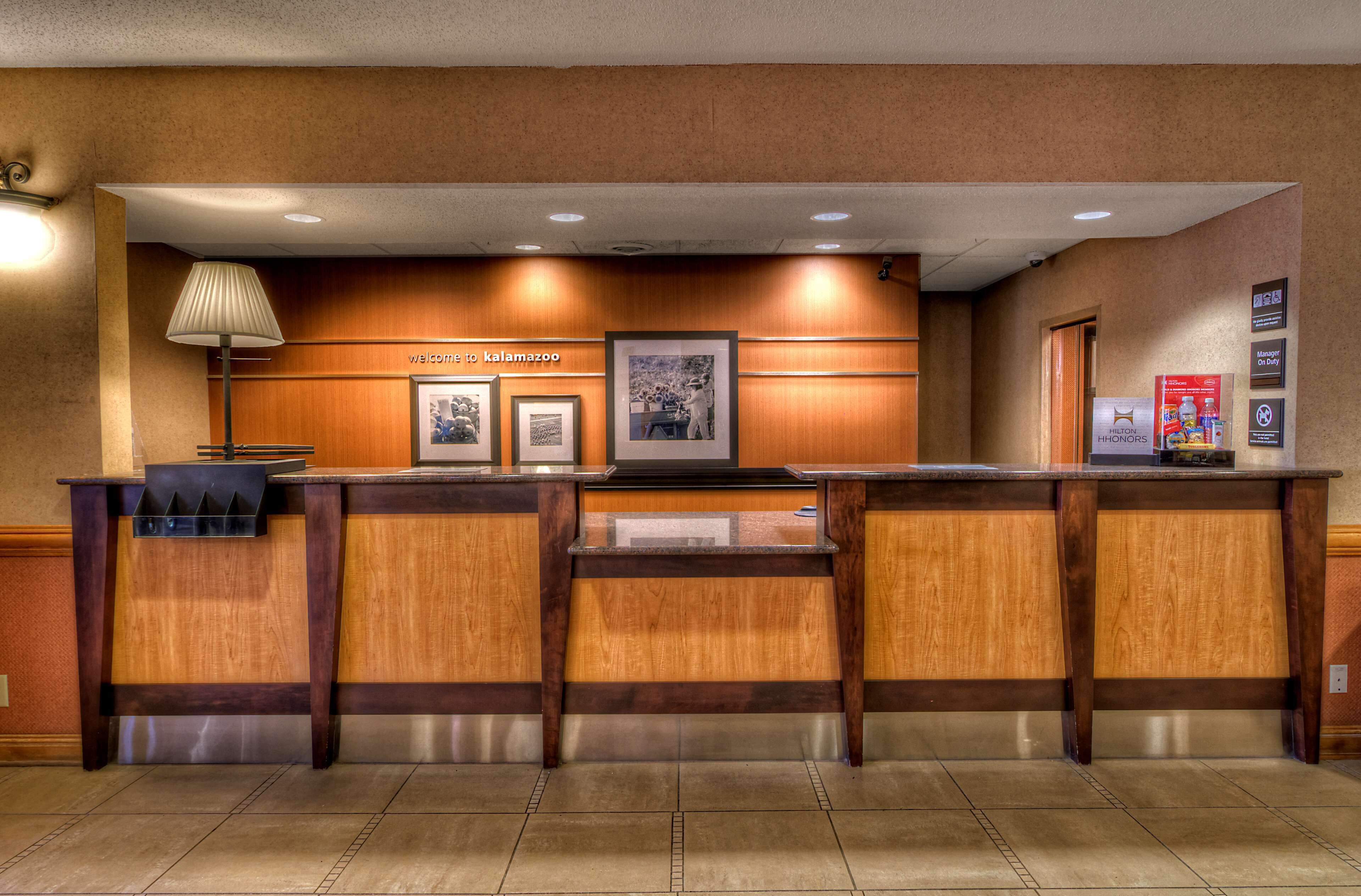 A reception desk with a wooden finish, framed pictures on the wall, and a sign that reads "Welcome to Alamazoo."