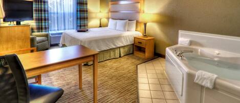 Habitación de hotel con cama, mesita de noche, lámpara, televisor, sillón y bañera.