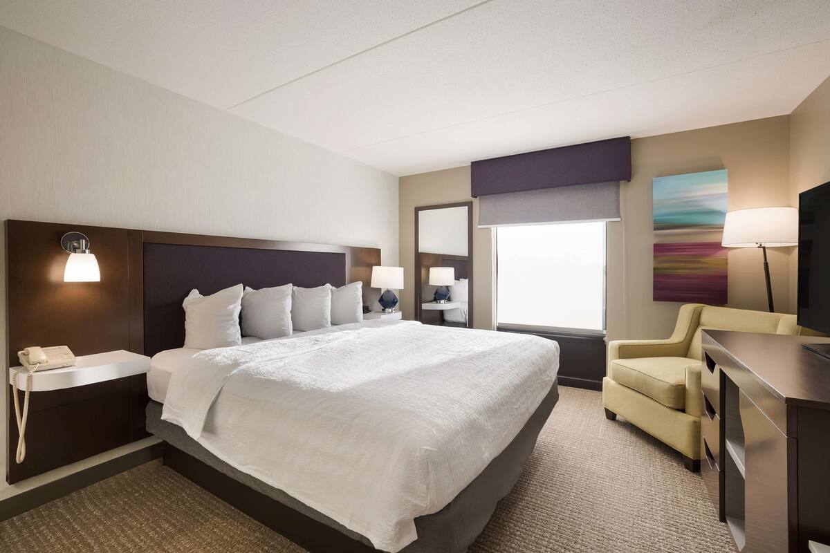 Een hotelkamer met een groot bed, nachtkastjes, een bureau, een stoel, een televisie en een raam met uitzicht.