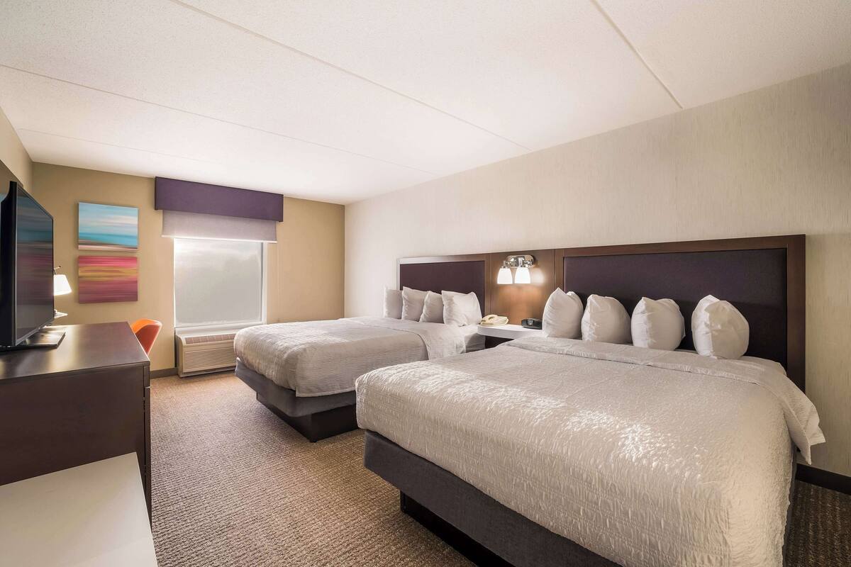 Hotelkamer met twee bedden, een bureau, een televisie en een raam met jaloezieën.
