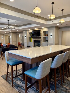 A spacious living area with a large island, bar stools, a flat-screen TV, and a fireplace. - Hampton Inn McHenry (McHenry)