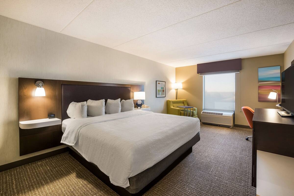 Een hotelkamer met een groot bed, nachtkastjes, een bureau, een stoel en een raam met uitzicht.
